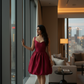 Woman in a red dress standing by a large window with a cityscape view.