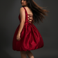 Woman in a red dress with a lace-up back against a dark background