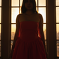 Woman in a red dress standing in front of a large window with a cityscape view.