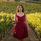 Woman in a red dress holding a glass of wine in a vineyard with a house in the background